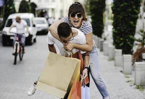 retrato de una alegre pareja joven caucásica hombre y mujer sosteniendo muchas bolsas de papel después de ir de compras mientras camina y habla en la calle. feliz pareja familiar con paquetes al aire libre. concepto de compra foto