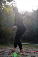 mujer equilibrando su caminata sobre una cuerda suelta atada entre dos árboles. mujer practicando cuerda floja caminando en un parque. foto