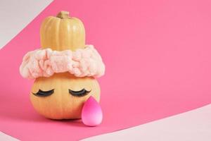 calabaza en una diadema y pestañas postizas sobre un fondo rosa, esponjas para aplicar maquillaje salón de belleza foto