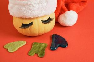 gau sha scrapers made of jadeite and a cute pumpkin with eyelashes and a santa hat on red background photo