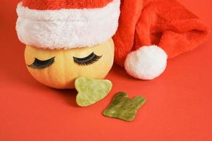 gau sha scrapers made of jadeite and a cute pumpkin with eyelashes and a santa hat on red background photo