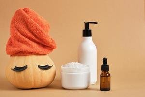 mock up set of cosmetic containers and pumpkin with towel and false eyelashes on beige background photo