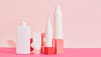 several different white plastic bottles and tube on pink geometric podiums on pink background photo