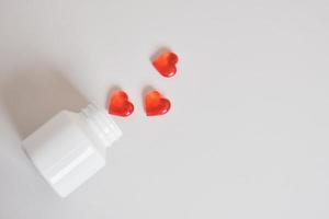 pastillas rojas en forma de corazones y tarro blanco. símbolo de amor. pastillas de amor Pastillas para la salud del corazón. foto