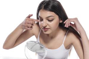 Portrait of a girl putting cosmetic ointment on face while watching at mirror indoor photo