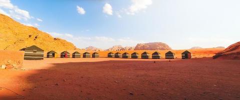 Wadi Rum desert, Jordan, 2022 - Beautiful aerial view of bedouin camp at sunset from above with tents lined up and red rock formations. Panoramic landscape photo