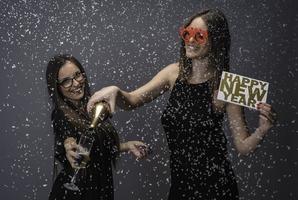 Two female friends celebrating New Year with confetti and champagne holding sign. isolated photo