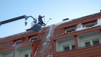 Worker on lift truck removing snow from the roof of the building, slow motion video