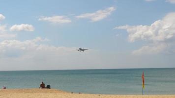 el avión está aterrizando desde el lado del mar. turistas en la orilla observan el aterrizaje del avión video