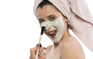 hermosa mujer joven con una toalla envuelta alrededor de su cabeza aplicando mascarilla de arcilla en el baño foto