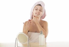 Attractive young adult woman apply facial cream look in mirror, beautiful healthy lady wrapped in towels put moisturizing lifting nourishing day creeme on soft hydrated moisturized skin in bathroom photo