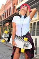 Beautiful hipster girl with skate board wearing sunglasses in the city. photo