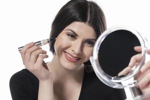 Portrait of a young woman applying liquid make up on her face. Isolated on white background photo