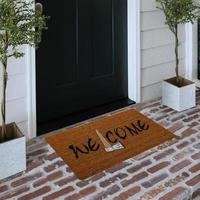 Designer Welcome Entry Doormat Placed on Solid Brick Floor Outside Entry Door with Plants photo