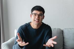 un joven asiático explica seriamente hablar en el sofá. videoconferencia en línea, entrevista de trabajo, reunión. foto