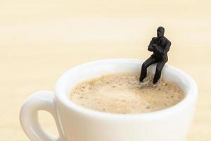 Businessman figurine sitting at a coffee cup. Coffee break concept photo