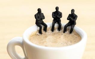 Group of businessman figurines sitting at a coffee cup talking to each other photo