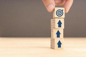 Business goal and objective target concept. Hand holding a cube with target icon and arrows on stacked blocks. Copy space photo