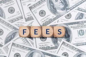 FEES word on wooden blocks and US dollar bills background photo