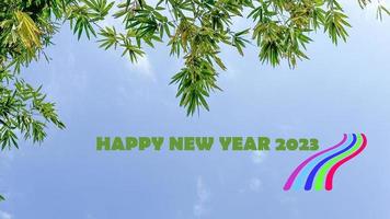 hojas de árbol sobre fondo de cielo azul con texto feliz año nuevo 2023 y gráfico de pequeñas líneas de colores foto