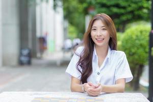 Portrait of an Asian Thai girl student in a uniform is sitting smiling happily and confidently in university photo