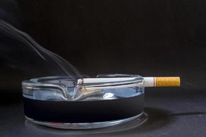 un cigarrillo con humo que se muestra contra un fondo negro foto