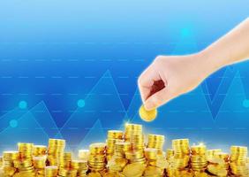 one hand is putting gold coins on pile of gold coins with graphic blue background photo