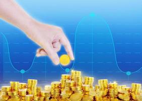 one hand is putting gold coins on pile of gold coins with graphic blue background photo