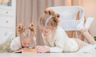 2 blonde girls lie on the floor by the Christmas tree and read a book. cozy evenings with a book by the tree. Girlfriends read a book together. Warm relationship photo