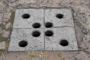 Balcony steel drain hole mesh and green leaves. Black metal Drainage grate for draining, directing excess water down into the sewers and prevent flooding. Dandelions sprouted between the tiles photo