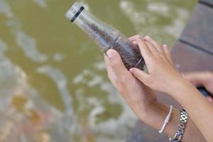 bebé y mano de la madre sosteniendo un frasco de comida para peces. foto