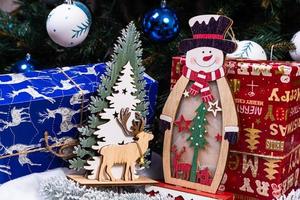 adornos navideños contra el fondo borroso. pequeño muñeco de nieve de madera. muñeco de nieve de madera rústica copo de nieve cerca de muñeco de nieve feliz sonriendo con los brazos arriba. tarjeta de felicitación de felices fiestas.