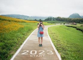 Happy new year 2023,2023 symbolizes the start of the new year. The letter start new year 2023 on the traveler woman photo shoot at road in nature fresh green tea and flowers farm mountain wallpaper.