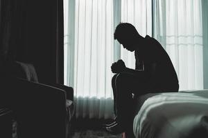 Silhouette depressed man sadly sitting on the bed in the bedroom. Sad asian man suffering depression insomnia awake and sit alone on the bed in bedroom. Depression health people concept. photo