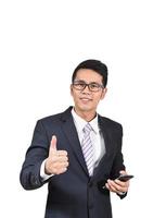 Asian business man smile wearing suit and glasses and thumbs up and holding mobile phone isolated white background. Business concept asian man chating with mobile or trading on mobile phone. photo