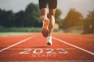 feliz año nuevo 2023 sport man runner corriendo hacia el nuevo año 2023. puesta en marcha de zapatos de pie de cerca para correr en el estadio ir a la meta del éxito. personas corriendo como parte del número 2023. cuidado de la salud deportiva. foto