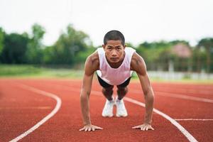 Athletes sport man runner wearing white sportswear to push up, stretching and warm up before practicing on a running track at a stadium. Athlete sportman prepare to training for competition race. photo