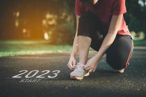 Sport woman runner tie shoelaces start into the new year 2023. Start up of runner woman running on nature race track go to Goal of Success. People running as part of Number 2023. Sport health care. photo