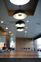 cierra el borde de la mesa de madera en el café con un fondo borroso de una moderna sala de diseño interior y una lámpara de iluminación foto