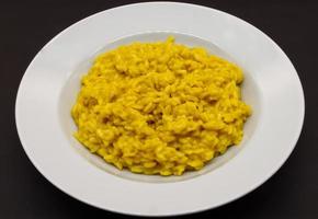 Italian Risotto allo Zafferano, rice with saffron, in a white dish isolated on black background photo