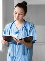 mujer médico persona usa uniforme y estetoscopio leyendo documento de información del paciente para consulta de cirugía. enfermera profesional asiática está trabajando como consulta de atención médica en el hospital foto