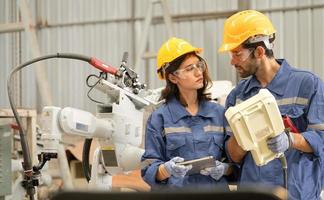 Male industrial engineer using remote control board to check robotic welder operation in modern automation factory. Woman technician monitoring robot controller system for automated steel welding. photo