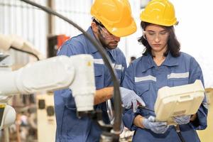 Female industrial engineer using remote control board to check robotic welder operation in modern automation factory. Technician man monitoring robot controller system for automated steel welding. photo