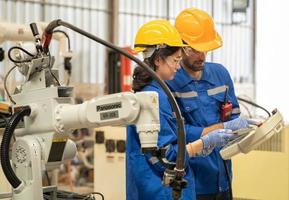 Male industrial engineer using remote control board to check robotic welder operation in modern automation factory. Woman technician monitoring robot controller system for automated steel welding. photo