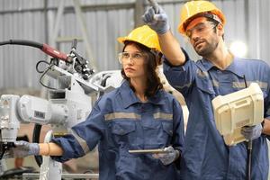 Male industrial engineer using remote control board to check robotic welder operation in modern automation factory. Woman technician monitoring robot controller system for automated steel welding. photo