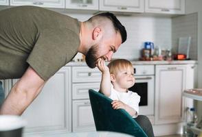 Happy father young man feeding and having fun with baby girl little daughter in kitchen at home photo