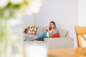 Young beautiful woman forty year with blonde long curly hair in cozy knitted grey sweater with cup of tea in hands in bright interior at home photo