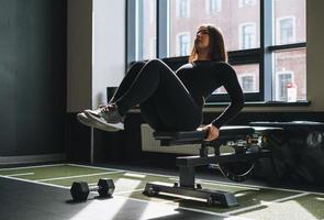 Young brunette woman training her muscles on bench in fitness club gym photo