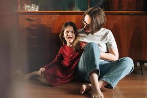 Emotional girl and her mother sitting on floor in living room at home photo