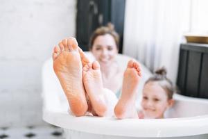 Young mother woman and little tween girl daughter having fun in bath with foam at home photo